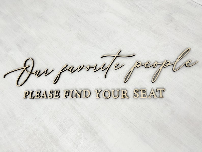 May include: A wooden sign with the text "Our favorite people" in cursive script and "Please find your seat" in block letters.
