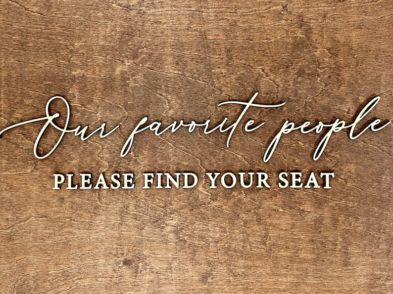 May include: A wooden sign with the text "Our favorite people, please find your seat" in white lettering.