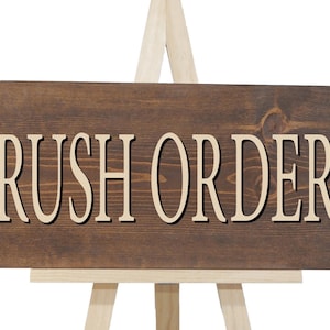 May include: A brown wooden sign with the text "RUSH ORDER" in white lettering. The sign is on a small easel.