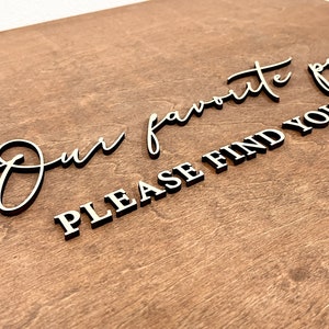 May include: A wooden sign with the text "Our favorite people please find your seat" in black lettering.