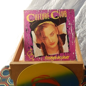 May include: A wooden crate containing a vinyl record. The record cover is purple and features a man with long hair. The record cover has the text "Culture Club" and "Kissing to be Clever".