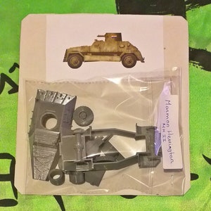 Puede incluir: Un kit de maqueta de plástico gris de un vehículo blindado Maammon Heunigton Mk II. El kit incluye el chasis, las ruedas y una torreta. El kit está empaquetado en una bolsa de plástico transparente con un respaldo de cartón blanco. El cartón tiene una imagen del vehículo blindado y el texto "Maammon Heunigton Mk II".