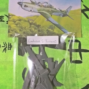 Può includere: Un kit di modellismo in plastica di un aereo Embraer EMB-312 Tucano. Il kit è in una busta di plastica trasparente e comprende più parti. Il kit è etichettato "Embraer S. Tucano."