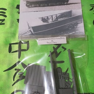 May include: A plastic model kit of a German World War II Landwasserschlepper, a type of amphibious vehicle used to transport supplies and troops across water. The kit includes multiple pieces, including the hull, the engine, and the wheels. The kit is packaged in a clear plastic bag with a label that reads "Landwasserschlepper # trailer".