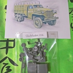 May include: A plastic model kit of a Studebaker US6 military truck. The kit includes multiple pieces, including the truck's chassis, wheels, and body. The kit is packaged in a clear plastic bag.