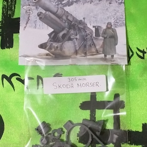 Puede incluir: Una bolsa de plástico que contiene un conjunto de piezas de modelo de plástico gris para un mortero Skoda de 305 mm. La bolsa está etiquetada con "305 mm SKODA MORSER."