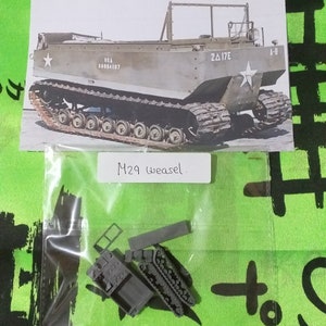 May include: A plastic model kit of a military vehicle, the M29 Weasel. The kit is in a clear plastic bag and includes several pieces, including the body, tracks, and a small rectangular piece. The kit is labeled "M29 Weasel."
