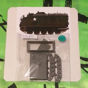 Op de afbeelding: Een modelbouwpakket van een N75 APC (Pantserwagen). De kit bevat ongemonteerde grijze plastic onderdelen, waaronder de carrosserie, de rupsbanden en andere componenten. Een afgedrukte afbeelding van het geassembleerde voertuig is zichtbaar boven de kit, met de tekst "tank encyclopedia".