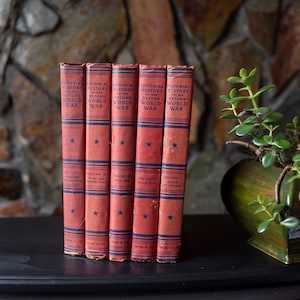 May include: A set of five red hardcover books titled " Pictorial History of the Second World War" with blue and white lettering and a star on the cover. The books are stacked on a black surface.