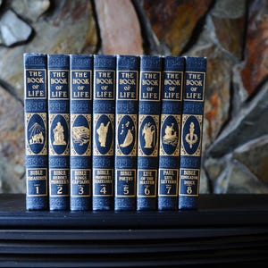 May include: A collection of eight vintage books titled "The Book of Life." The books have navy blue covers with gold lettering and illustrations. The spines display the title and volume numbers, with additional text at the bottom.