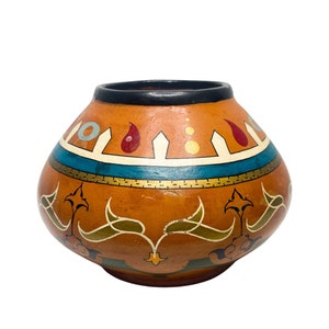May include: A round, orange ceramic vase with a black rim and intricate painted designs in gold, blue, green, and red. The vase has a traditional, ethnic style.