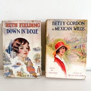 May include: Two vintage paperback books with colourful covers. The book on the left is titled "Ruth Fielding Down in Dixie" and the book on the right is titled "Betty Gordon in Mexican Wilds". Both books feature illustrations of young women in period clothing.