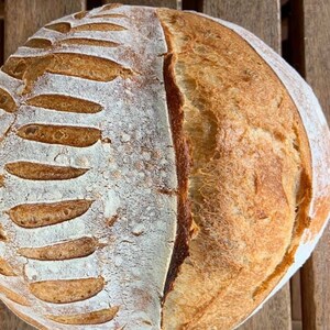 May include: A freshly baked loaf of sourdough bread with a scored crust. The bread has a light brown color and a slightly rough texture.