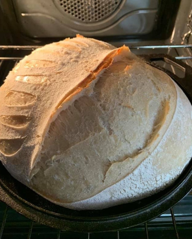 May include: A freshly baked loaf of sourdough bread with a crispy crust and a soft, airy interior. The bread is in a black cast iron pan.