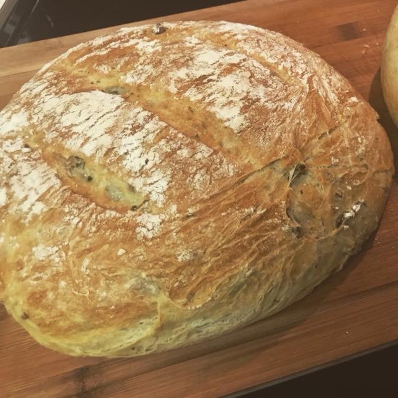 May include: A large, round loaf of bread with a golden brown crust and a slightly cracked surface. The bread is dusted with flour and has a few visible air pockets.