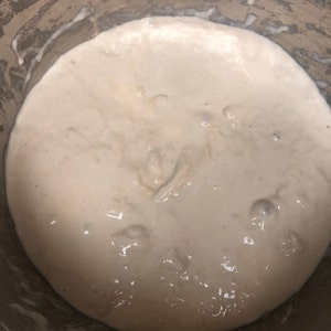 May include: A close-up of a white, bubbly dough mixture in a stainless steel pot.