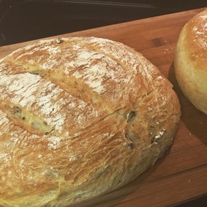 May include: Two loaves of freshly baked bread on a wooden chopping board. The bread is golden brown and has a crusty exterior.