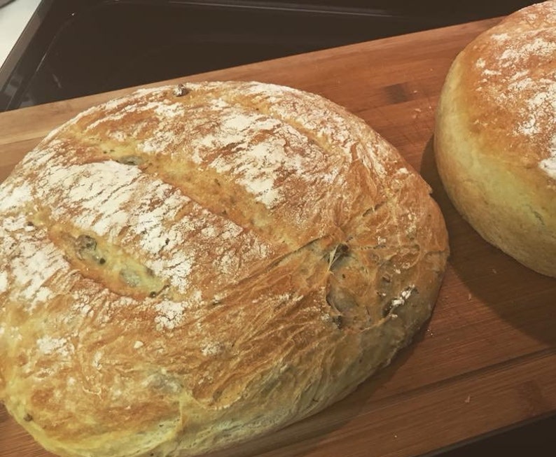 May include: Two loaves of freshly baked bread on a wooden chopping board. The bread is golden brown and has a crusty exterior.