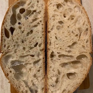 May include: A close-up of a sliced loaf of bread, revealing a light brown, airy crumb with large holes. The bread has a slightly irregular shape and a rustic appearance.