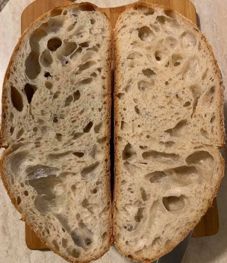 May include: A close-up of a sliced loaf of bread, revealing a light brown, airy crumb with large holes. The bread has a slightly irregular shape and a rustic appearance.