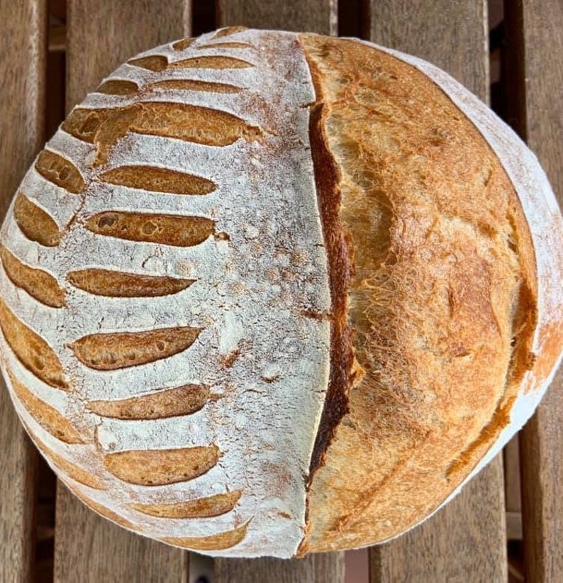 May include: A freshly baked loaf of sourdough bread with a distinctive pattern on the crust. The bread is golden brown and has a slightly crispy texture.