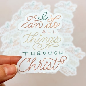 May include: White sticker with the text "I can do all things through Christ" in a cursive font. The words "I can do" are in teal, "all things" are in beige, and "through Christ" are in a light brown color. There are small hearts in the text.
