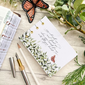 May include: A small white journal with a green and brown floral design and a butterfly illustration. The journal has gold eyelets and the text "You will seek me and find me when you search for me with all your heart." is written in calligraphy.