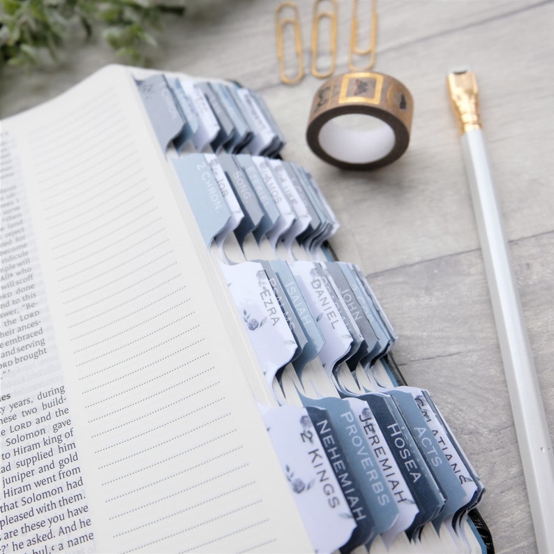 May include: A close-up of a Bible with blue and white tabs marking different books of the Bible, including John, Daniel, Isaiah, Ezra, Acts, Galatians, Hosea, Jeremiah, Proverbs, 2 Kings, and Nehemiah.