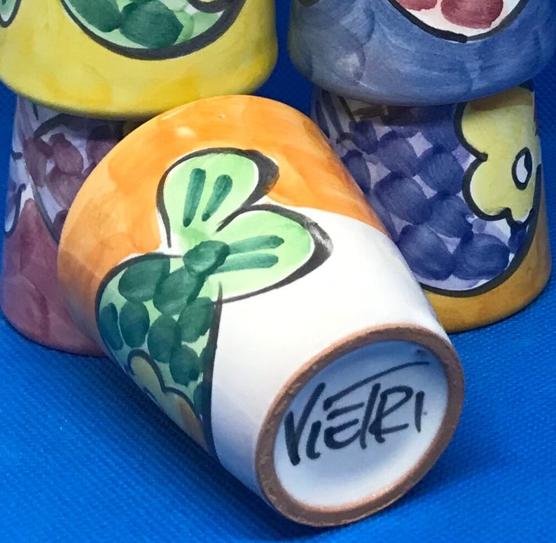 May include: A set of five small ceramic cups with colorful hand-painted designs. The cups feature a variety of floral and abstract patterns in shades of yellow, orange, blue, green, and purple. The bottom of one cup is signed "VIERI".