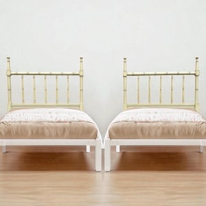 May include: Two twin-sized beds with bamboo-style headboards and white frames. The headboards are a light beige color, and the beds are covered with a light brown blanket and a patterned comforter. The beds are set against a white wall.