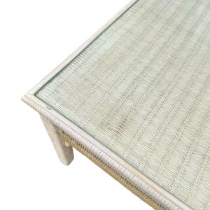 May include: A rectangular coffee table with a woven rattan base and a glass top. The table has a light beige color and a natural, textured appearance. The table is approximately 40 inches long, 20 inches wide, and 18 inches high.