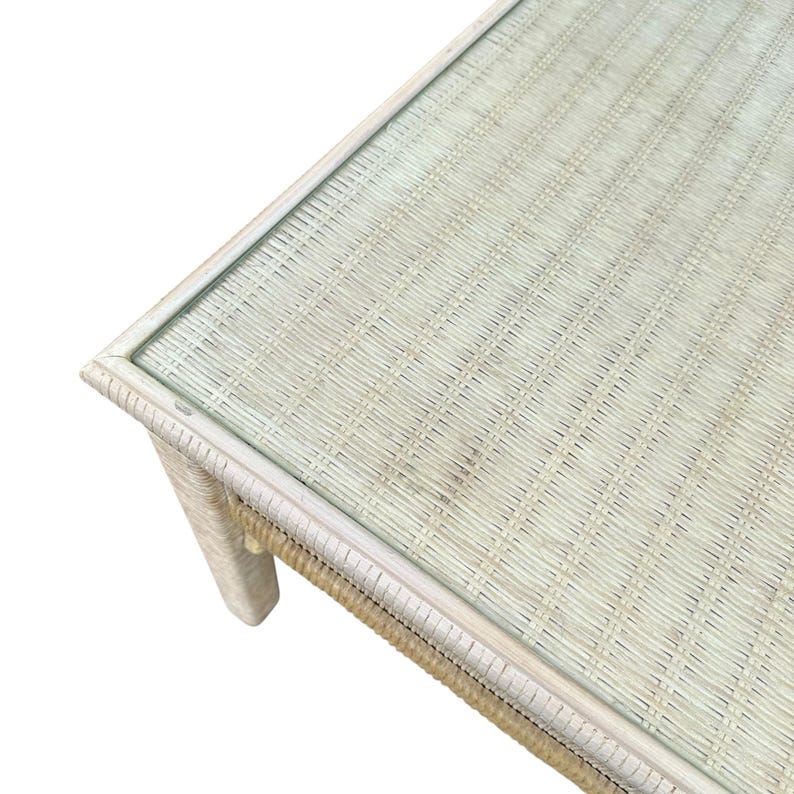 May include: A rectangular coffee table with a woven rattan base and a glass top. The table has a light beige color and a natural, textured appearance. The table is approximately 40 inches long, 20 inches wide, and 18 inches high.