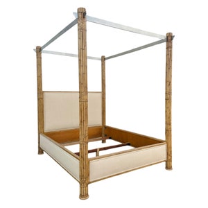May include: A four-poster bed with a bamboo-style frame. The bed frame is a light brown color, with a rectangular headboard and footboard upholstered in a cream-colored fabric. The bed has a canopy frame made of silver metal.