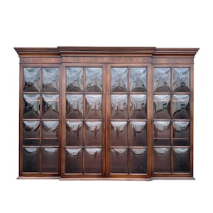 May include: A large, dark wood cabinet with four glass-paned doors. The glass is divided into small, square sections. The cabinet has a decorative top and base. The wood has a rich, warm tone, suggesting a classic or antique style.