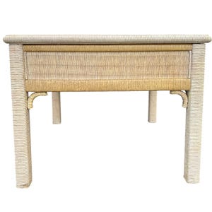 May include: A rectangular side table with a woven rattan design. The table features a light beige color with a drawer in the center. The legs are square and the table is approximately 30 inches long, 18 inches wide, and 24 inches high.