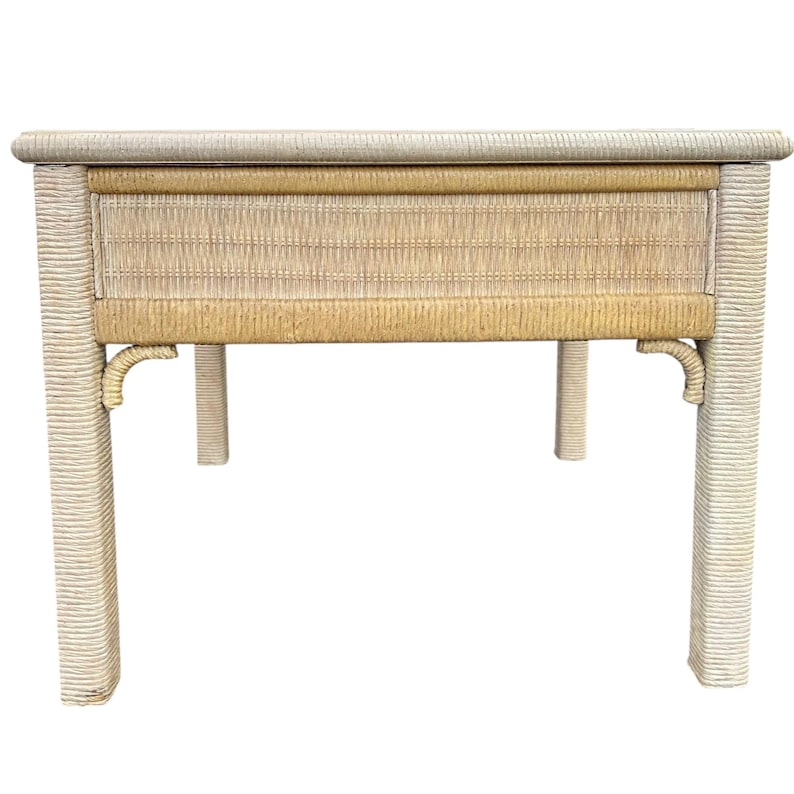May include: A rectangular side table with a woven rattan design. The table features a light beige color with a drawer in the center. The legs are square and the table is approximately 30 inches long, 18 inches wide, and 24 inches high.