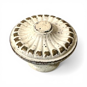 May include: Cream-colored ceramic cabinet knob with a decorative, ridged top and a speckled finish. The knob features a dark brown trim and accents, adding a vintage or antique aesthetic. Ideal for furniture restoration or adding a unique touch to cabinets.