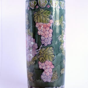 以下が含まれることがあります： ピンクと紫のブドウが描かれた花柄の緑色の陶器の花瓶。光沢のある仕上げと白い縁取りが施されています。