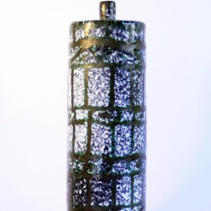 May include: A tall, cylindrical ceramic vase with a textured surface. The vase features a dark green and blue pattern with a grid-like design. The top has a small, cylindrical stopper. The vase is approximately 12 inches tall.