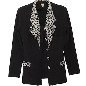 May include: A black blazer with a white and black animal print collar and lapel. The blazer has three buttons and matching animal print accents on the pockets. The jacket is hanging on a hanger.