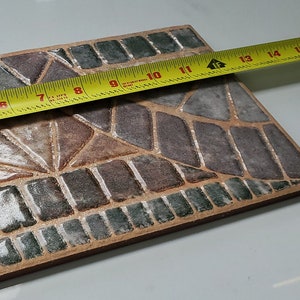 May include: A rectangular tile with a mosaic pattern of brown, green, and white. The tile is measured with a yellow tape measure, showing a length of 28 cm.