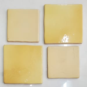 Könnte beinhalten: Vier quadratische Keramikfliesen in verschiedenen Gelbtönen. Die Fliesen sind in einem Gittermuster angeordnet.