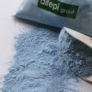 Puede incluir: Una bolsa de polvo de lechada azul con la etiqueta "difeppi grout" en ella. El polvo se derrama de la bolsa sobre una superficie blanca.