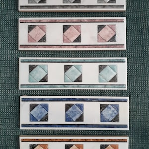 Puede incluir: Cinco tiras de borde de baldosas cerámicas con fondo blanco y un patrón repetido de tres formas de diamante. Las formas de diamante son de diferentes colores: gris, rosa, azul claro, azul y naranja.