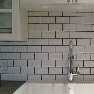 May include: A white porcelain kitchen sink with two basins and a chrome faucet. The sink is installed in a countertop with white metro tiles as a backsplash.