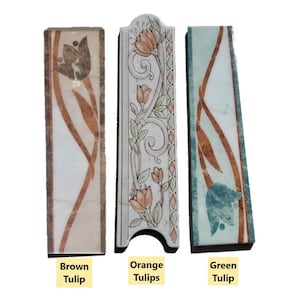 Puede incluir: Tres piezas de moldura de azulejos decorativos con diseños florales. El azulejo de la izquierda tiene un diseño de tulipán marrón, el azulejo del medio tiene un diseño de tulipán naranja y el azulejo de la derecha tiene un diseño de tulipán verde.