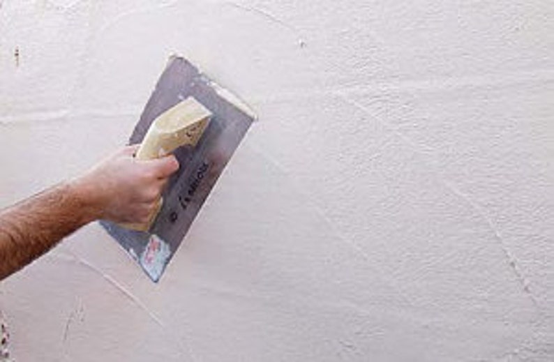 May include: A person using a trowel to apply a layer of white plaster to a wall.