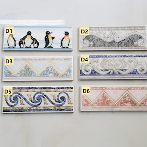 May include: Six different tile border designs. The first tile border features a row of penguins. The second tile border features a grey and white floral design. The third tile border features a blue and white chevron design. The fourth tile border features a blue and white floral design. The fifth tile border features a blue and gold swirl design. The sixth tile border features a pink and gold chevron design.