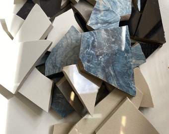May include: A pile of broken ceramic tiles in various shades of gray, blue, and white. The tiles are irregular in shape and size, and some have a marbled pattern.