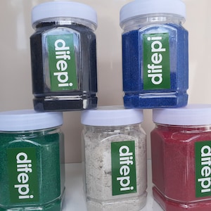 Könnte beinhalten: Fünf Glasbehälter mit weißen Deckeln, gefüllt mit Sand in verschiedenen Farben. Jedes Gefäß hat ein grünes Etikett mit dem aufgedruckten Wort "difeppi". Die Gefäße sind in Pyramidenform angeordnet.